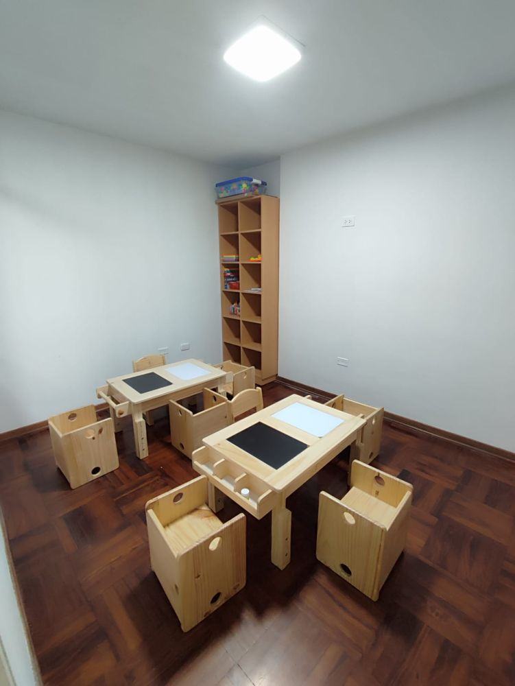 Aula con mesas de madera con pizarra y estante de material didáctico