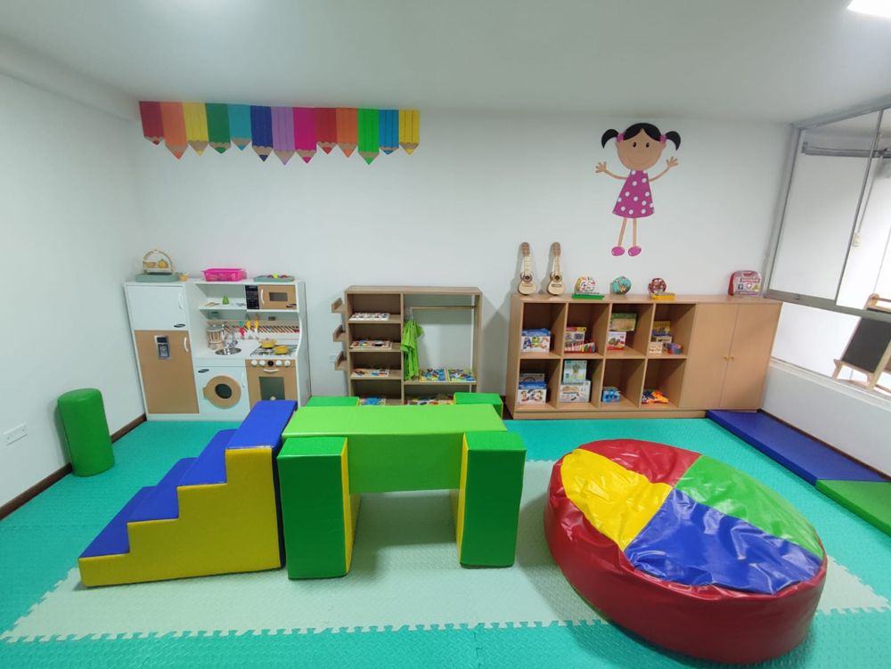 Sala de juegos del centro con cocina, estantes de material didáctico y bloques de espuma